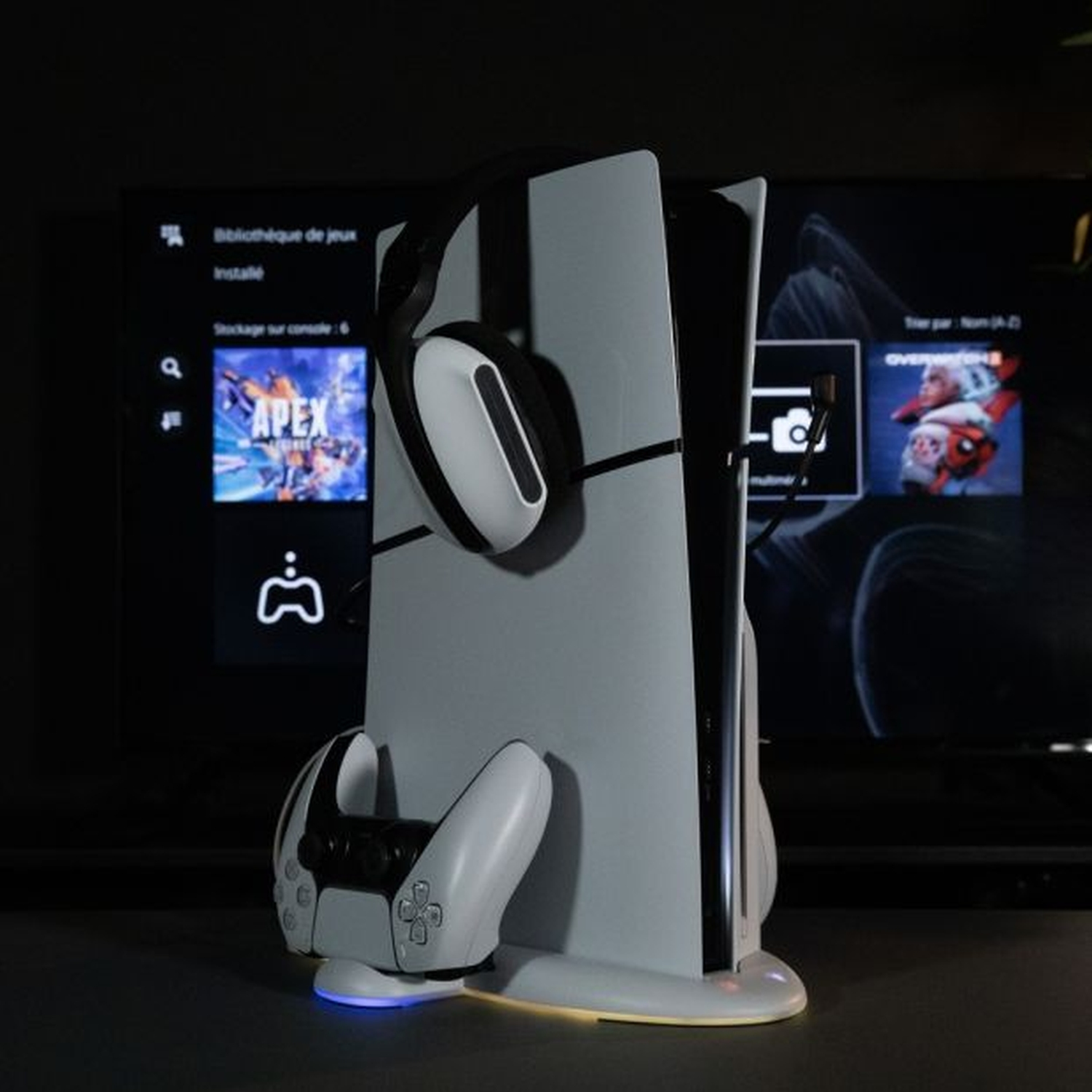 Configuration de jeu avec une PS5, un support de manette et un casque. La TV affiche un jeu.