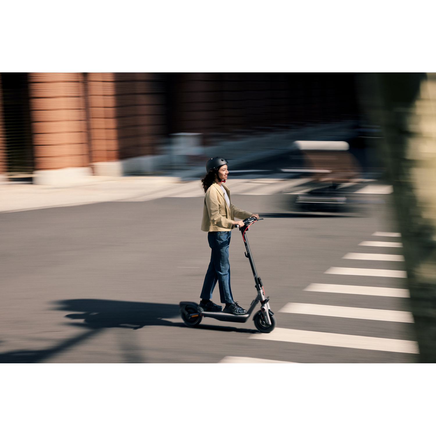 A person riding a black and gray scooter on a street with a blurred background.
