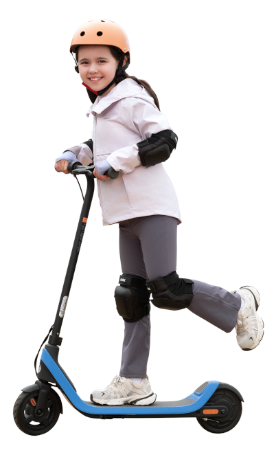 Dziewczyna na hulajnodze, w kasku i ochraniaczach, uśmiecha się do kamery.