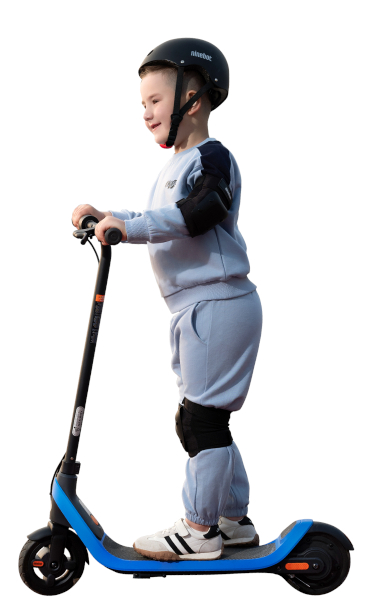 Chłopiec na hulajnodze, w kasku i ochraniaczach, uśmiecha się.