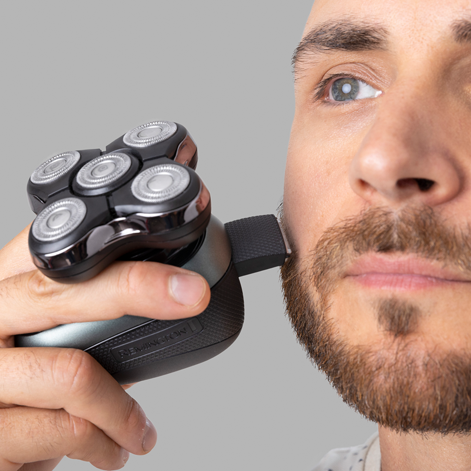 Een man scheert zijn baard met een elektrisch scheerapparaat. Het scheerapparaat is zwart en grijs.
