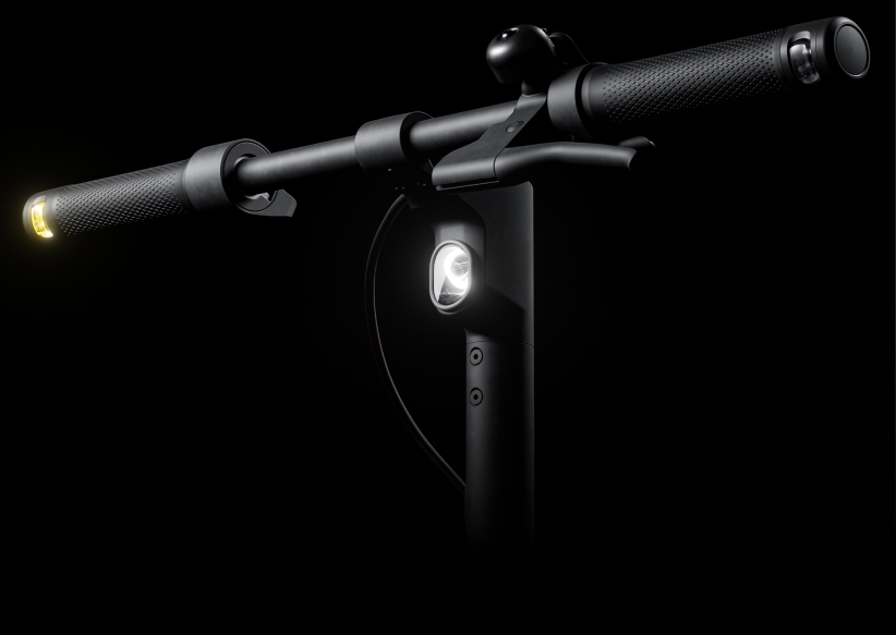 Zbliżenie kierownicy i światła hulajnogi elektrycznej na czarnym tle.