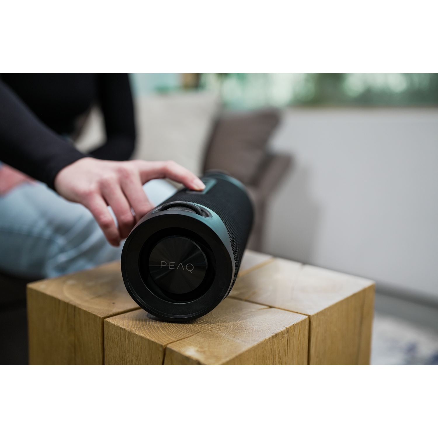 Zwarte cilindrische speaker op houten blok, hand in de buurt.