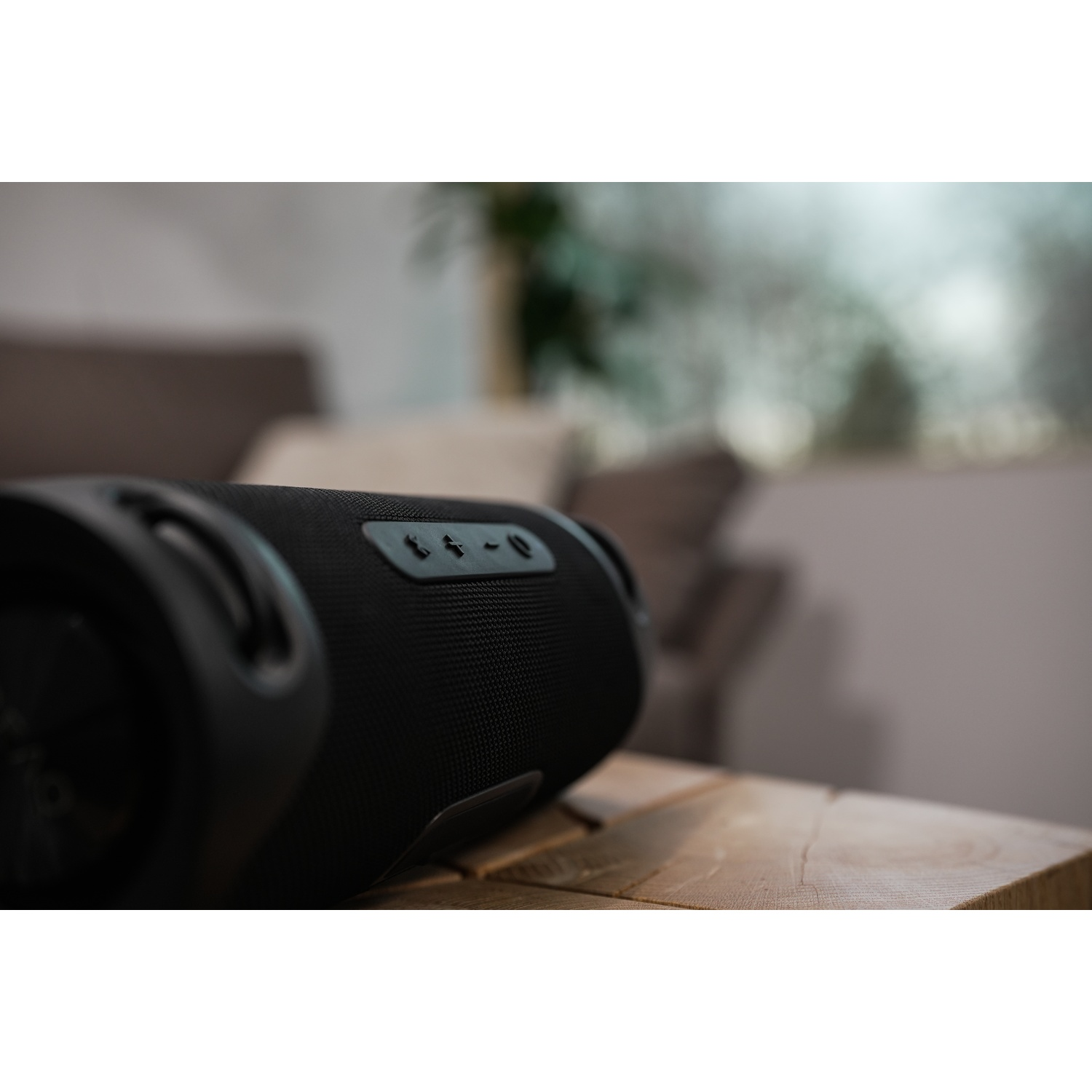 Zwarte speaker op een houten tafel in een woonkamer. Knoppen zijn zichtbaar aan de bovenkant.
