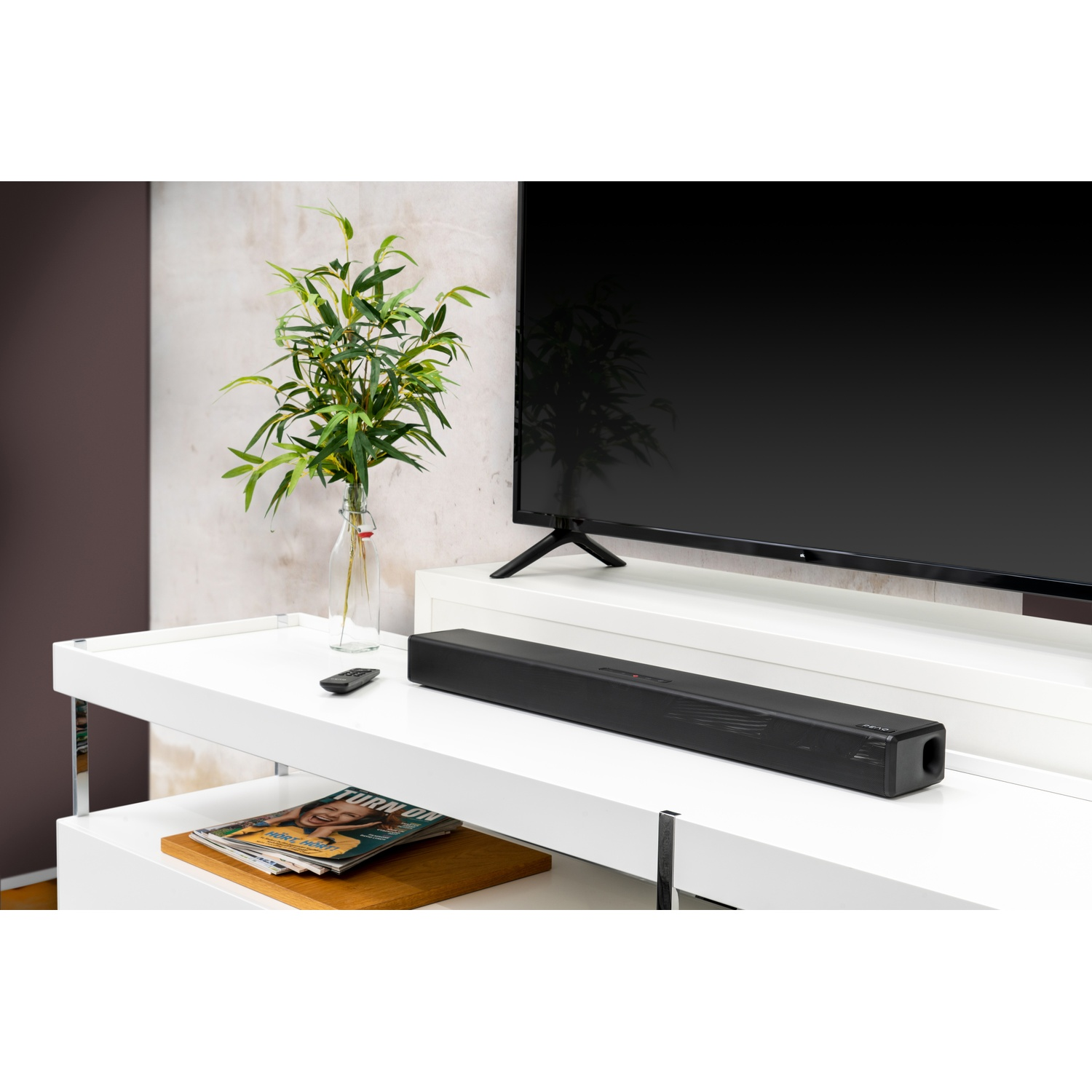 Een zwarte soundbar, tv en decoratie op een witte plank.