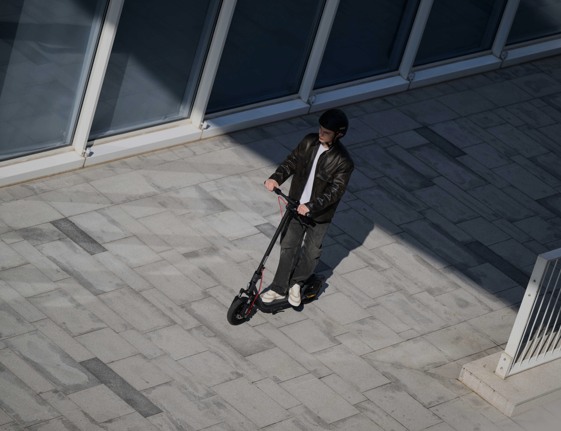 Widok z góry na mężczyznę jadącego hulajnogą elektryczną po utwardzonym terenie.