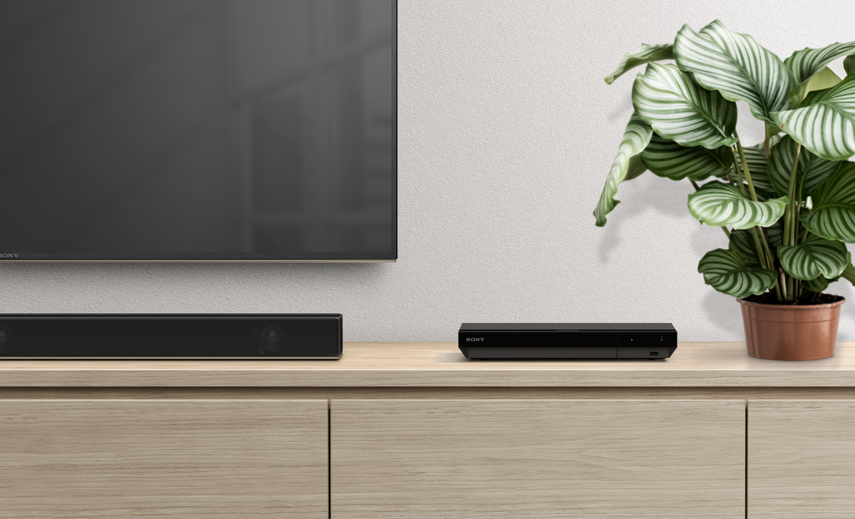 Fernseher, Soundbar, Mediaplayer und Pflanze auf einem Holzschrank.