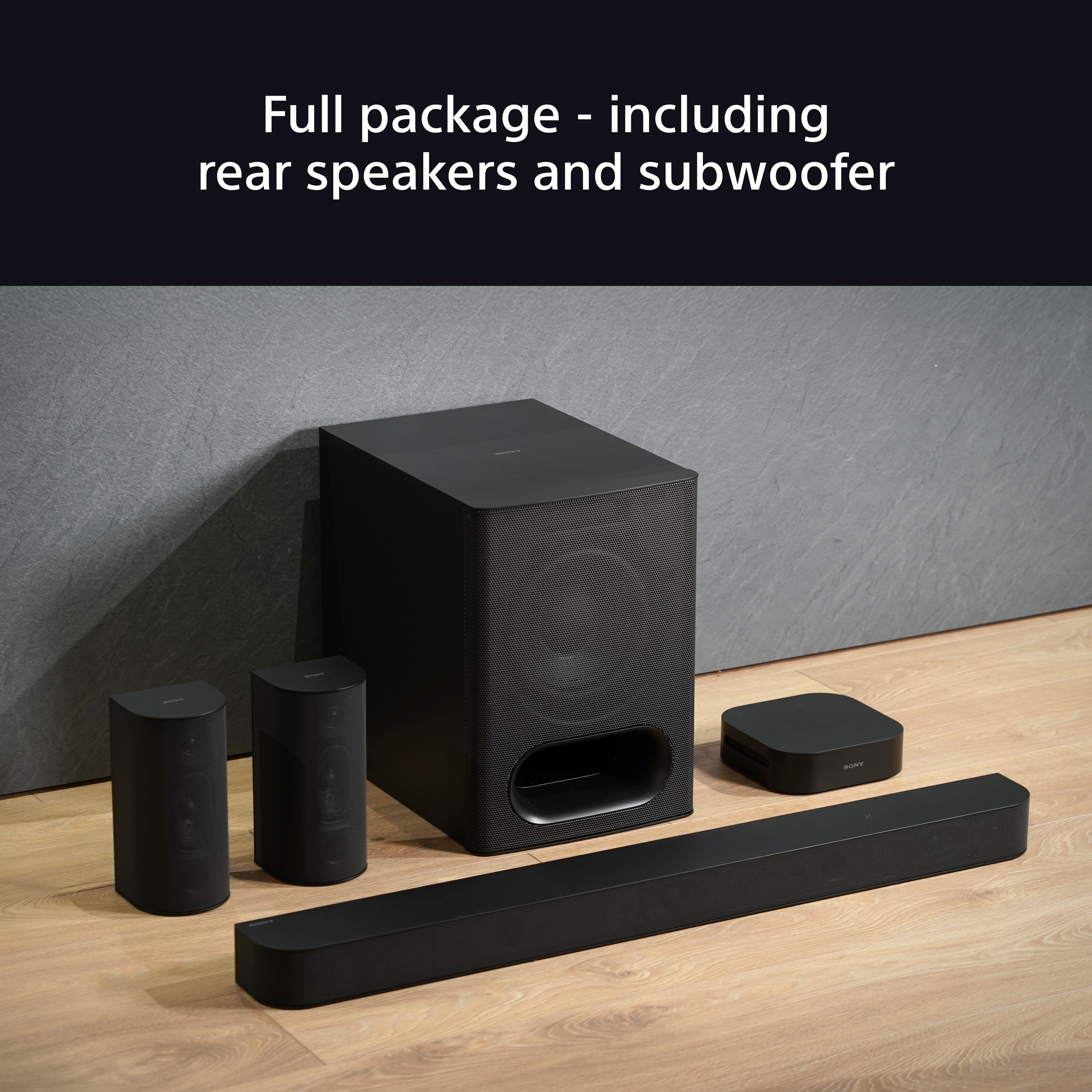 Système de son surround noir complet. Deux petits haut-parleurs, un caisson de basses et une barre de son sur plancher en bois.