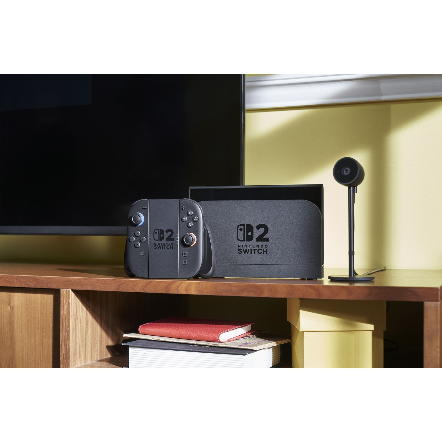 Una console di gioco con controller e un supporto. È posizionata su una superficie di legno, vicino a una TV.