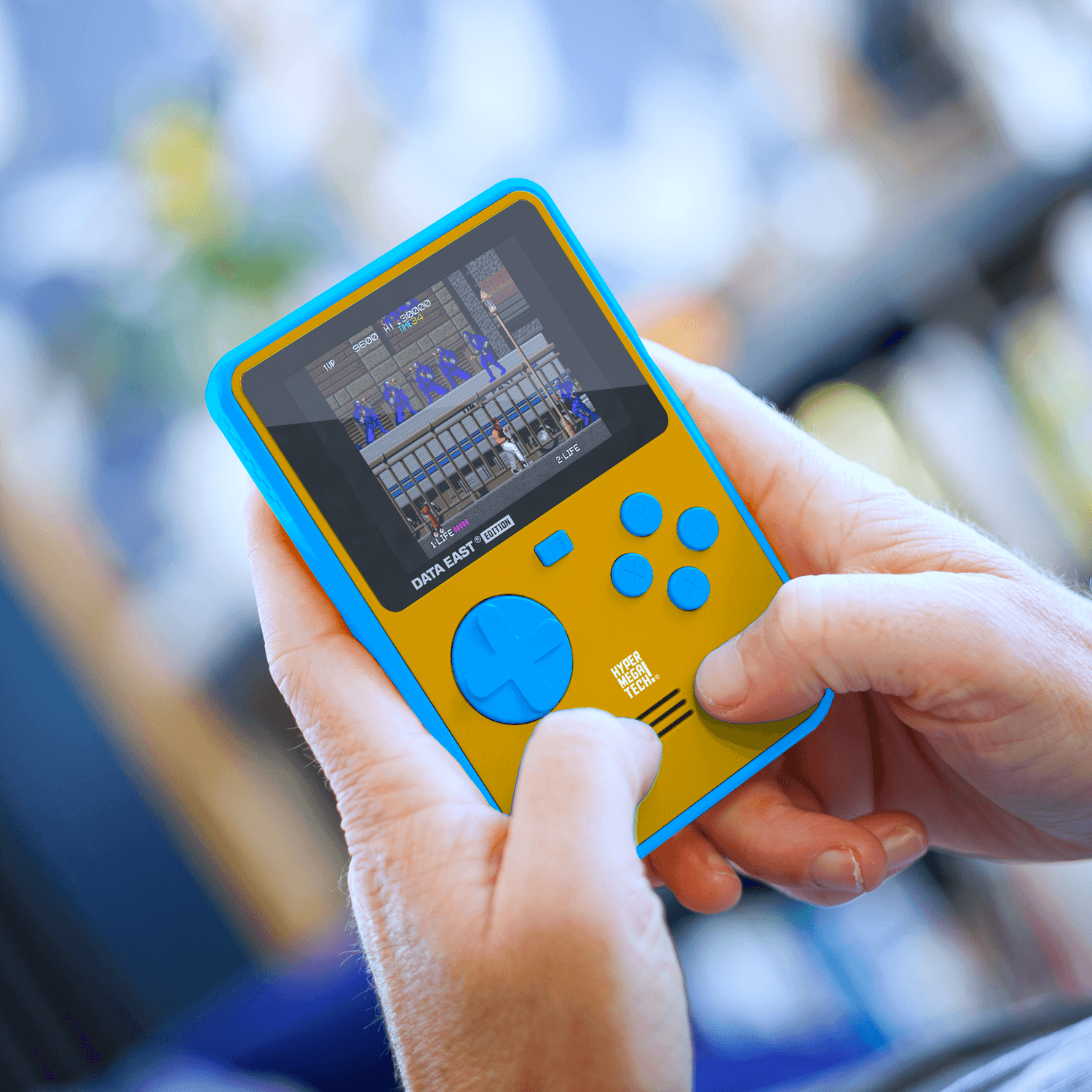 Osoba trzyma żółto-niebieskie przenośne urządzenie do gier, wyświetlające ekran gry z niebieskimi przyciskami.