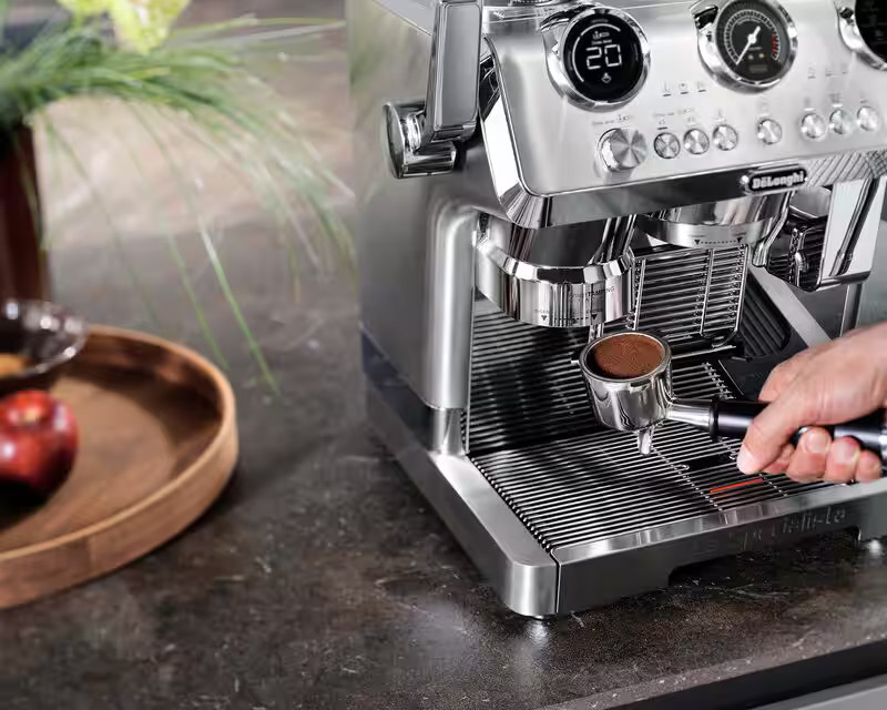 Ekspres do kawy ze stali nierdzewnej. Ręka trzyma kolbę.