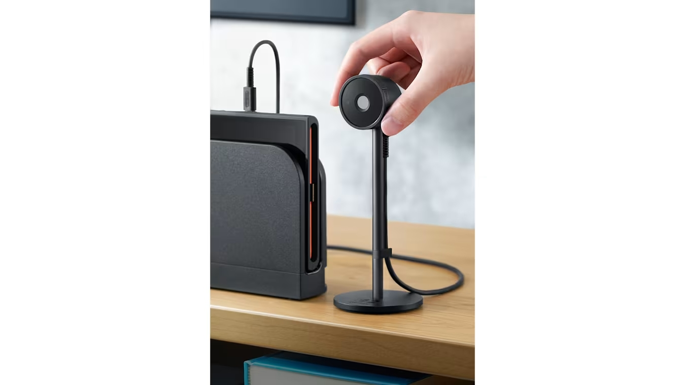 Una mano colocando un accesorio negro de Nintendo Switch en una base negra. Se ve un escritorio.