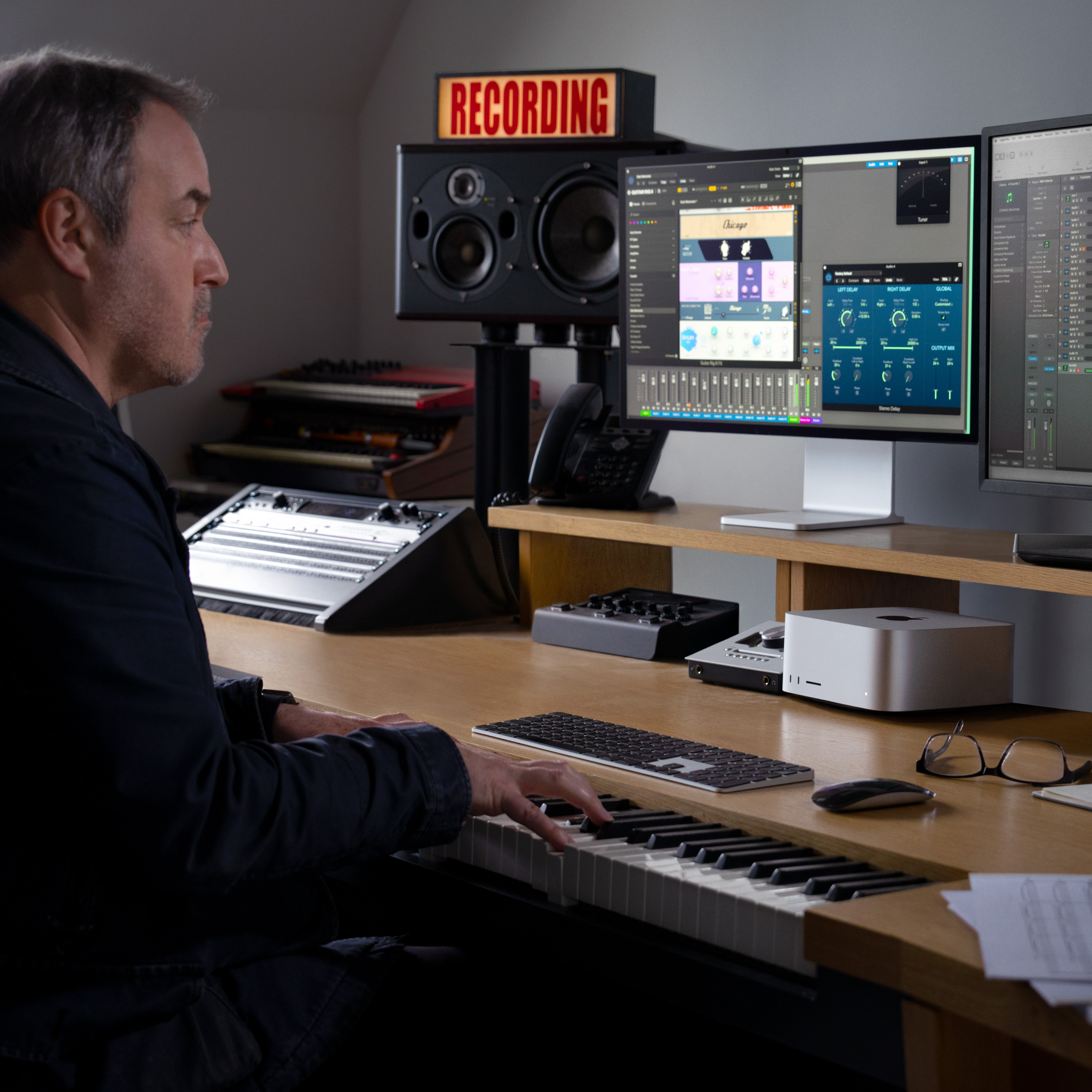 Hombre en estudio de grabación, tocando teclado con varias pantallas de ordenador.