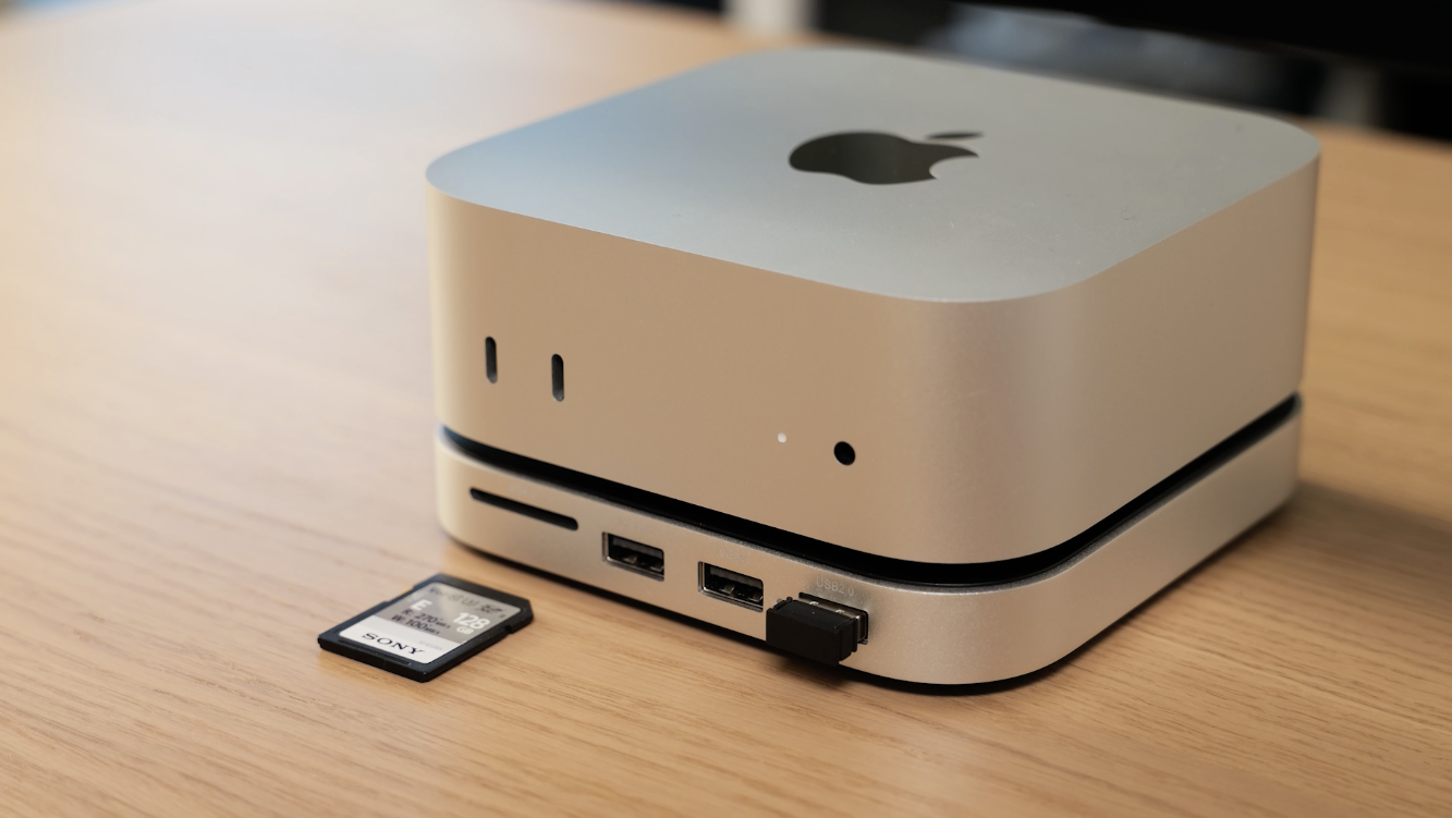 Ein silberner Apple Mac Mini mit einer SD-Karte und einem USB-Laufwerk auf einem Holztisch.