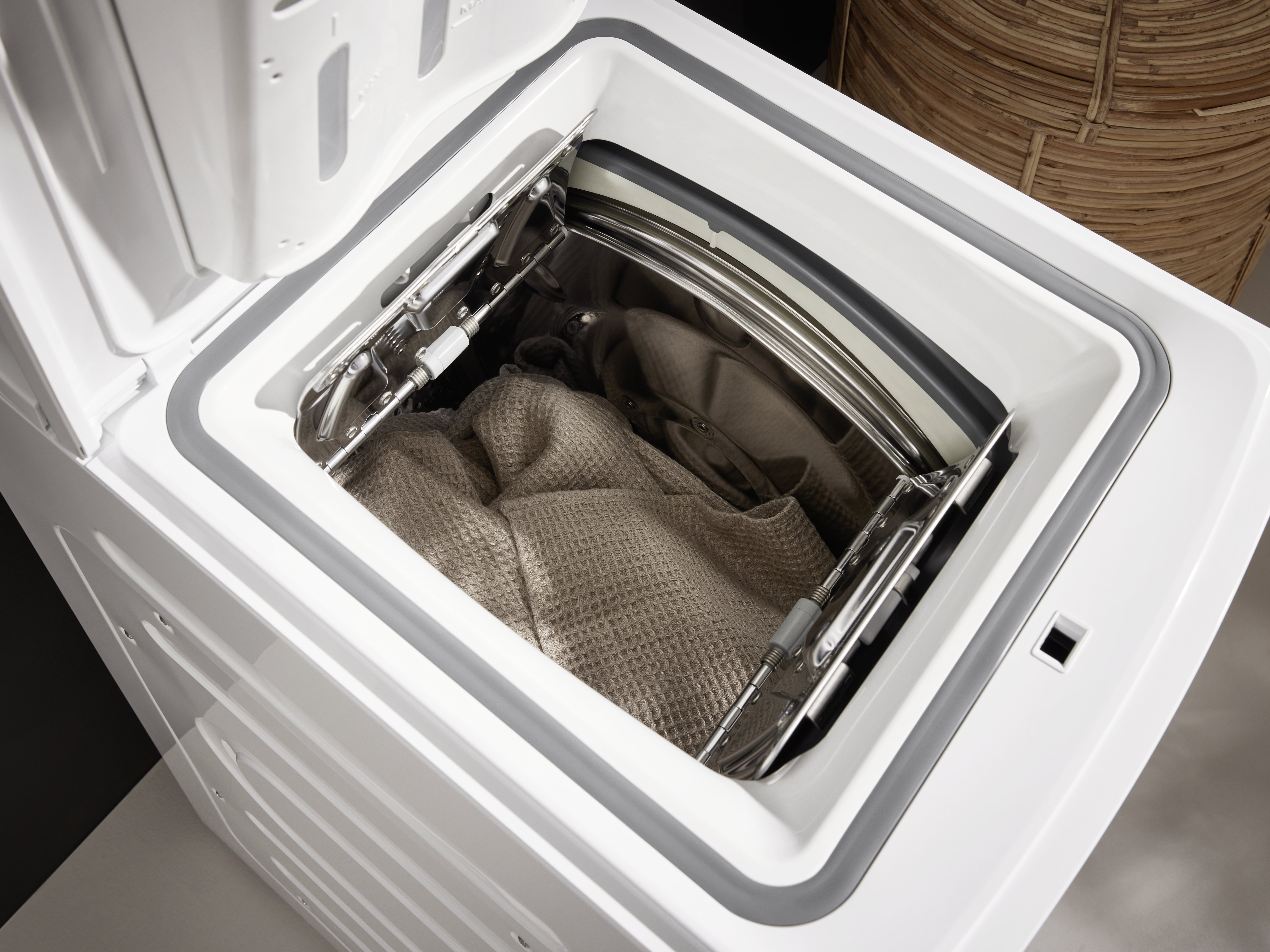 Offene weiße Waschmaschine mit Kleidung. Der Hintergrund ist ein geflochtener Korb.