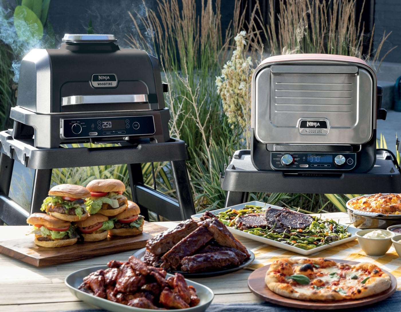 Grillek és főtt ételek egy asztalon a szabadban: hamburgerek, bordák, pizza és köretek.