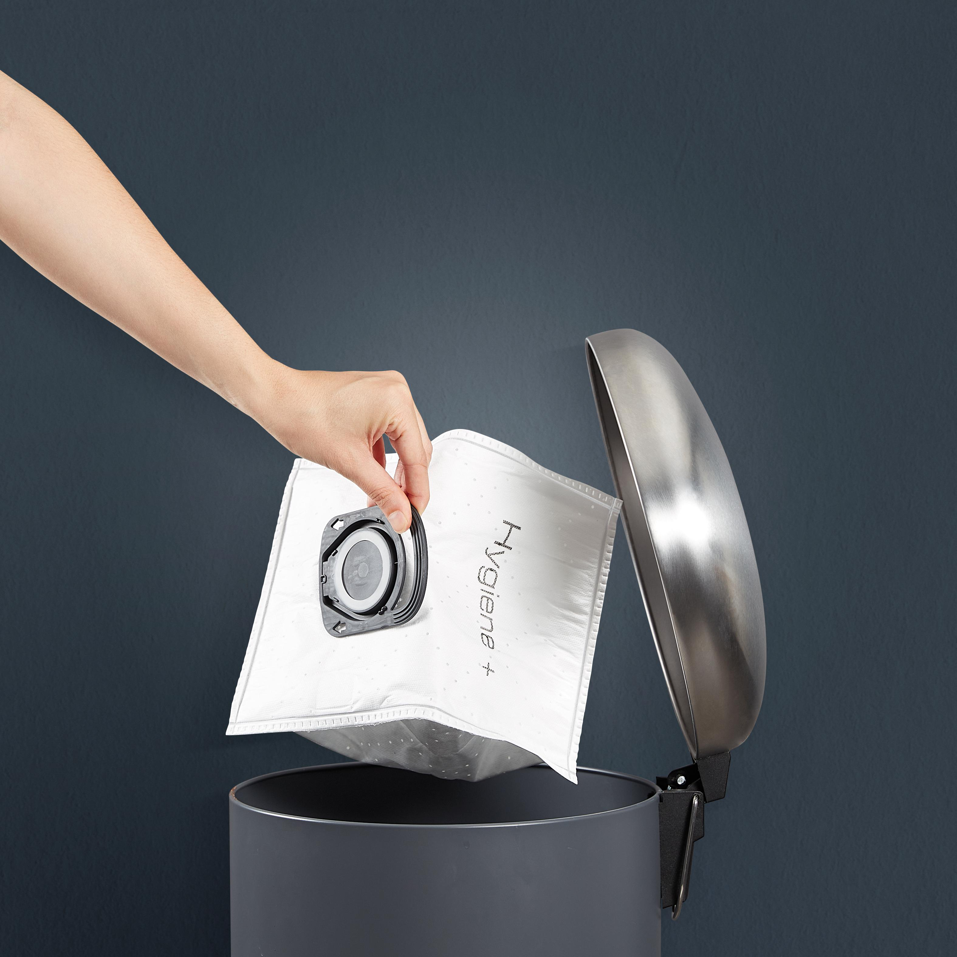 Eine Hand legt einen Staubsaugerbeutel in eine graue Tonne. Auf dem Beutel steht 'Hygiene+'.