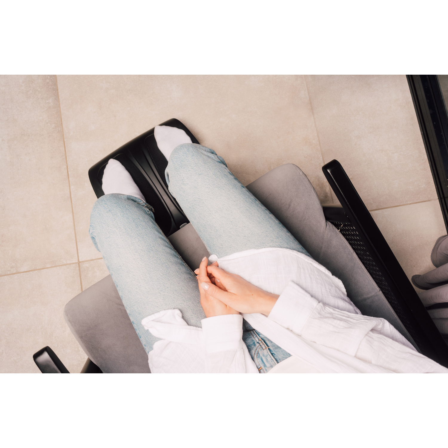 Person's legs and hands resting on a footrest and chair.