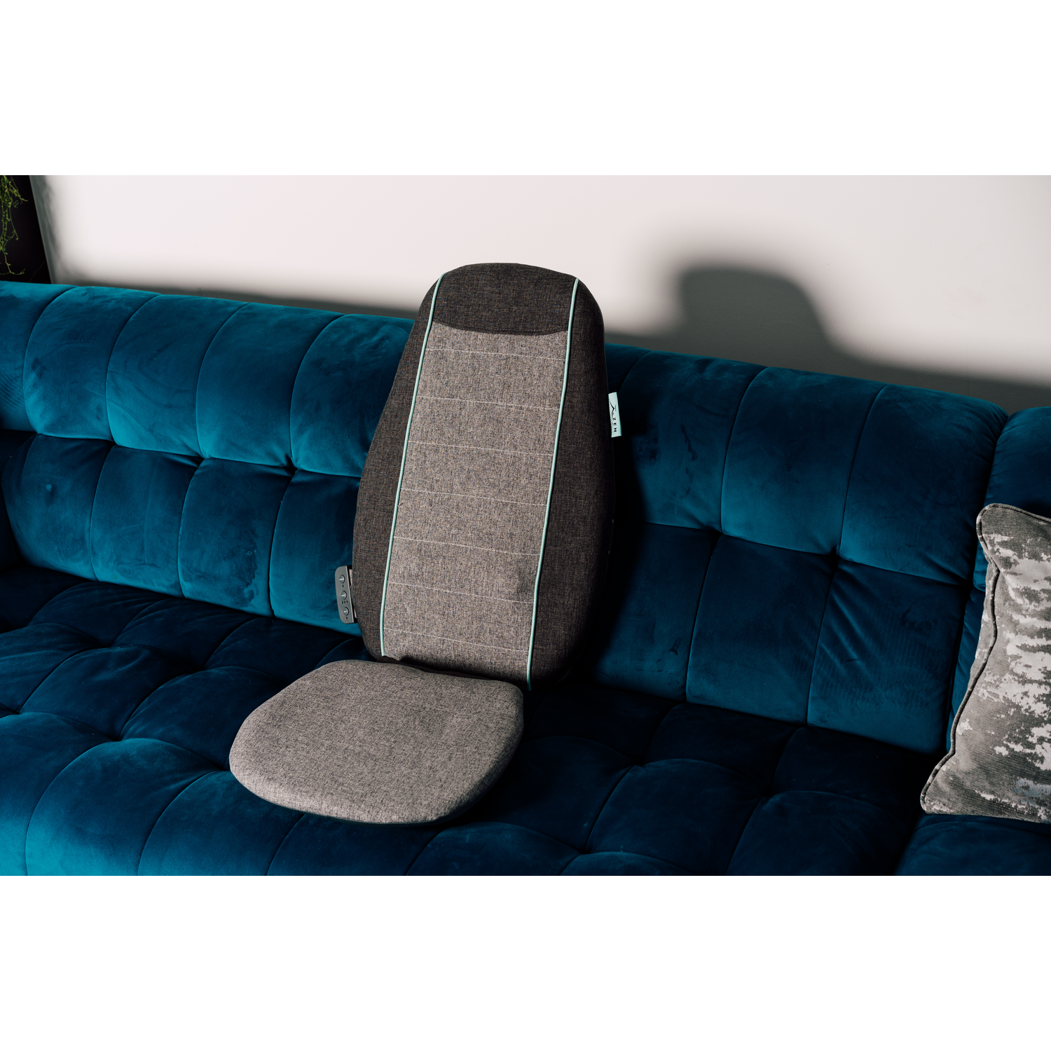 Un masseur de dos gris et bleu sur un canapé bleu, avec un oreiller gris à droite.