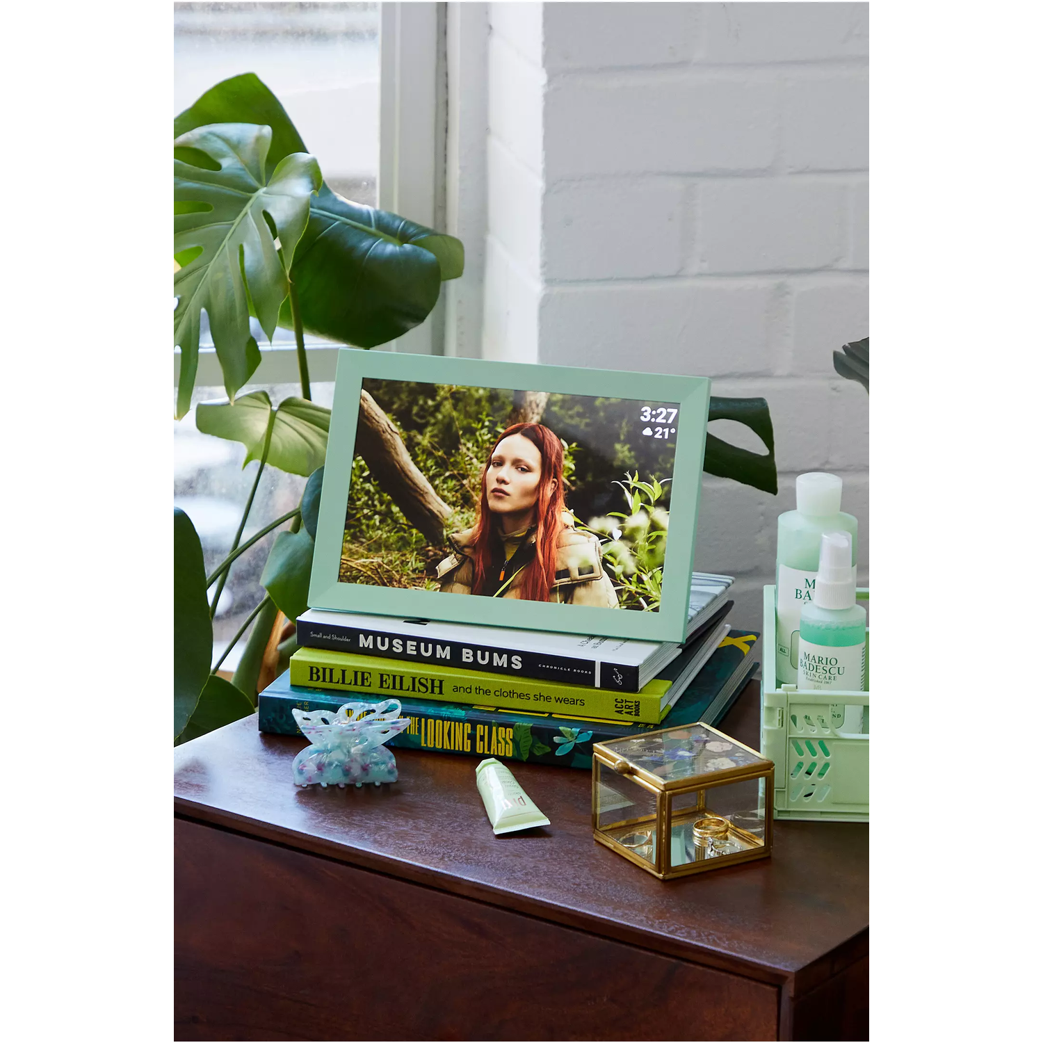 A framed digital photo displaying a woman, with books and a small glass box on a wooden table.
