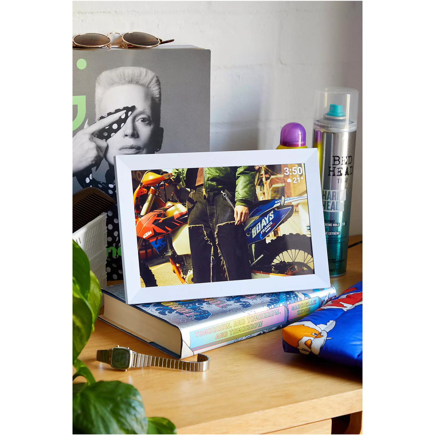Frame showing a motorcycle image. Other items include a book, sunglasses, and a plant.