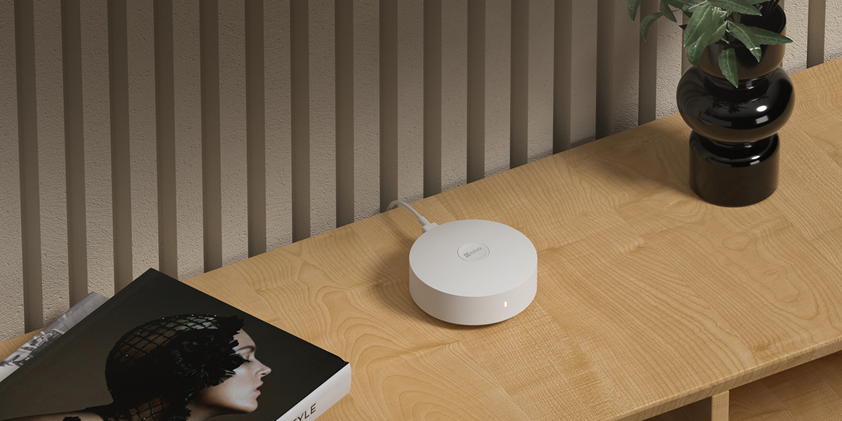 Un router de internet blanco sobre una mesa de madera. Una planta y un libro también en la mesa.