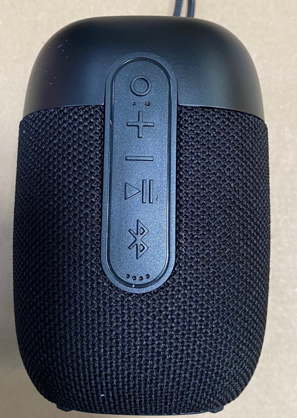 Czarny głośnik cylindryczny z przyciskami sterowania i siatkową tkaniną pokrywającą jego obudowę.