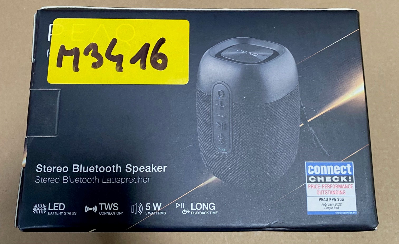 Pudełko głośnika stereo Bluetooth z naklejką. Czarny głośnik na pudełku. Widoczny tekst i logo.