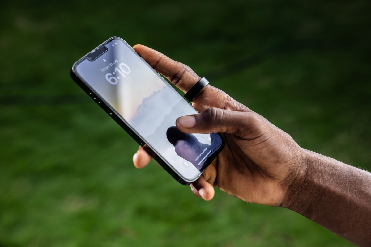 Die Hand einer Person, die ein Telefon mit einem Ring am Finger hält.