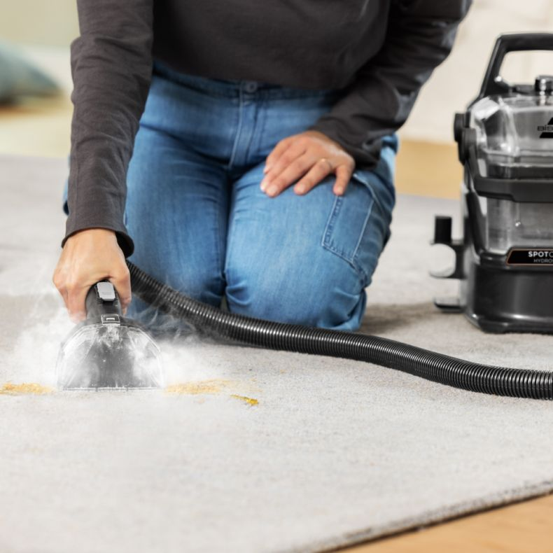 Osoba używająca Bissell SpotClean do czyszczenia dywanu roztworem czyszczącym.