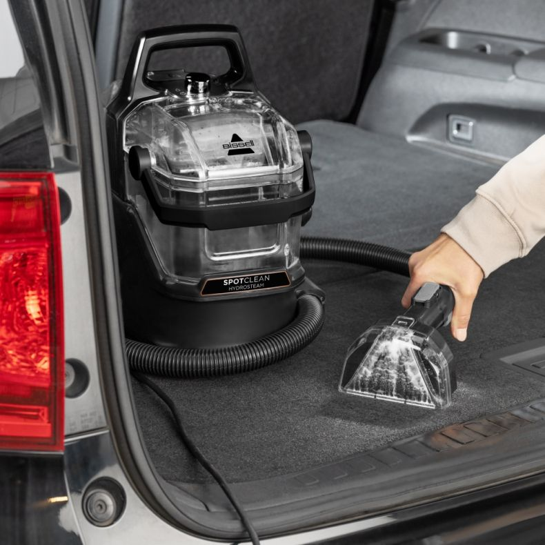 Urządzenie czyszczące z przezroczystym wierzchem czyści wnętrze samochodu. Tło jest rozmyte.