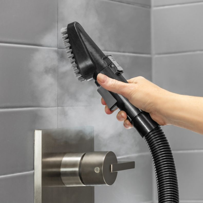 Czarna i szara głowica parownicy trzymana jest przez dłoń. Wylatuje para.