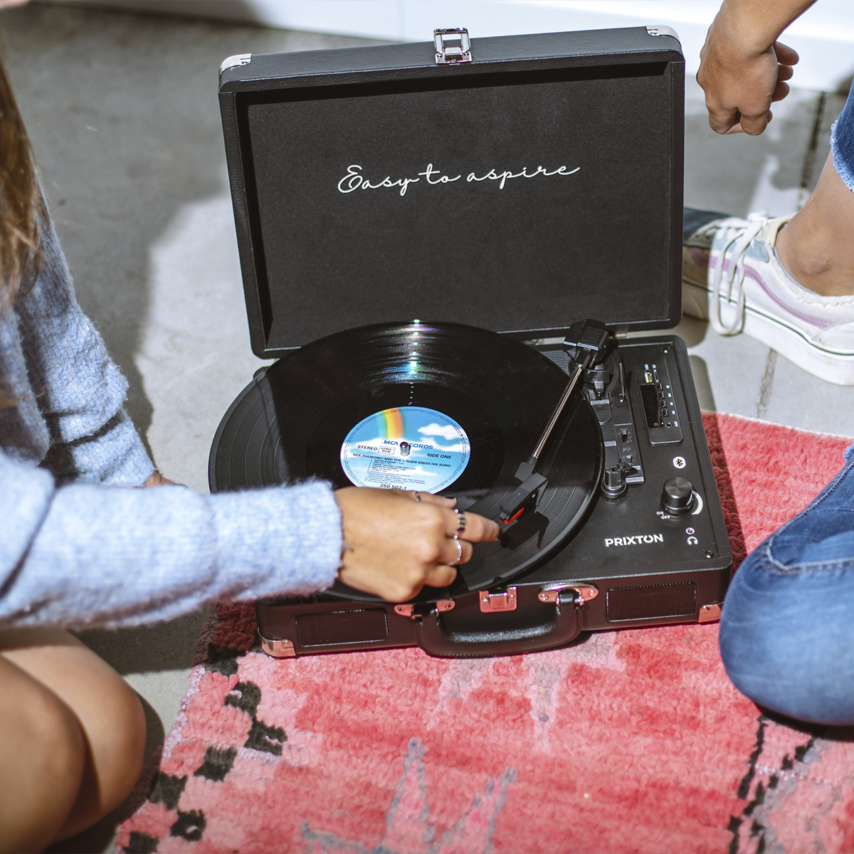 Un tocadiscos reproduciendo un disco. Dos personas sentadas en el suelo cerca del tocadiscos.