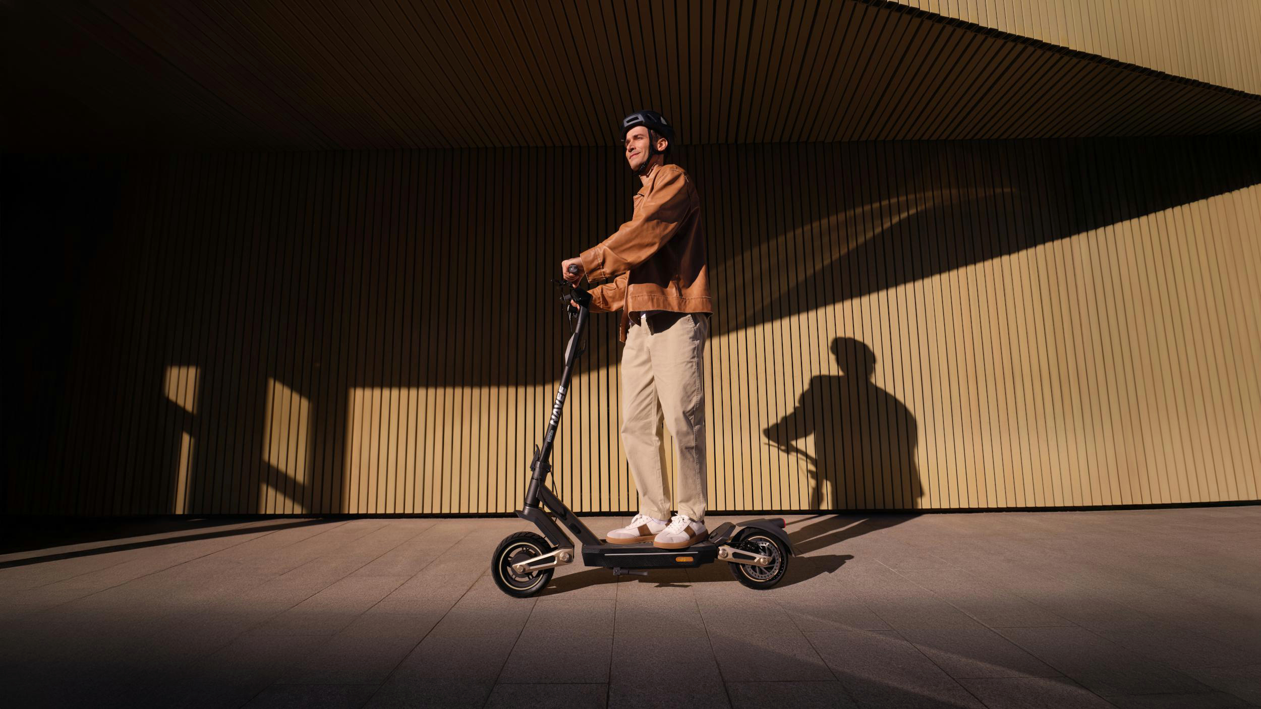 Mann auf einem Roller mit Helm, fährt auf einem Weg.