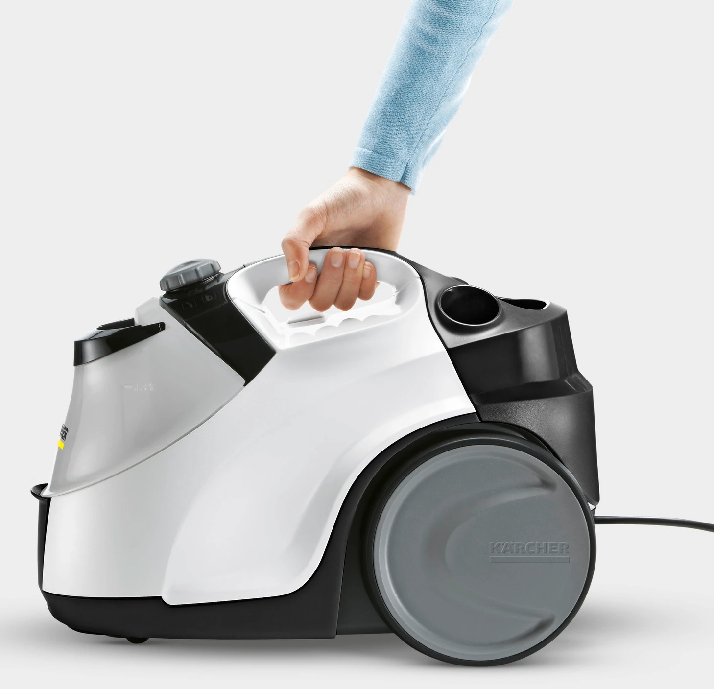 Osoba trzymająca biało-czarny odkurzacz parowy. Szare koło z boku. Jasne tło.
