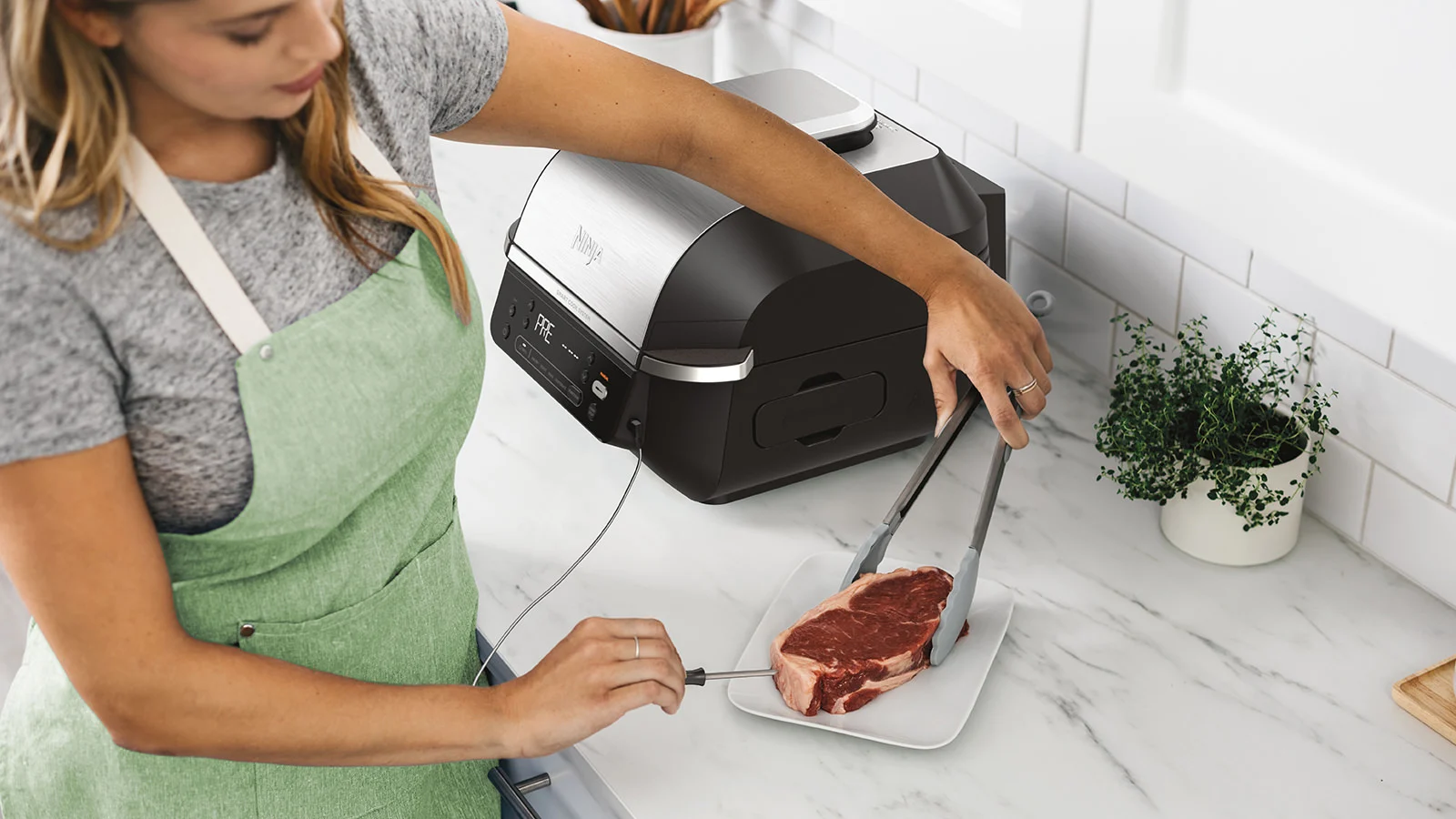 Nő csipesszel helyez egy steaket a tányérra, egy grill mellett.