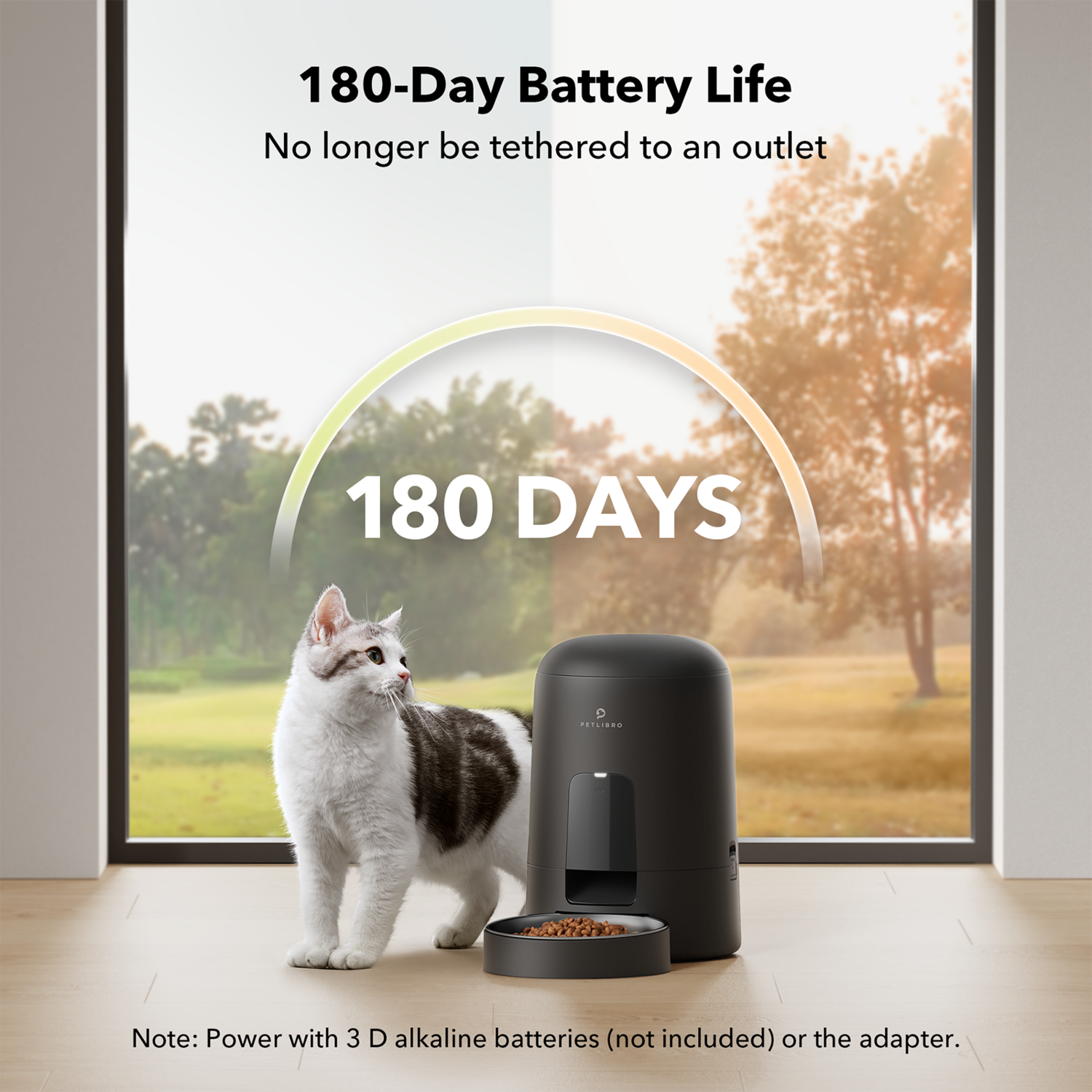 Een kat en een zwarte voederautomaat bij een raam. Tekst: 180 dagen batterijduur.