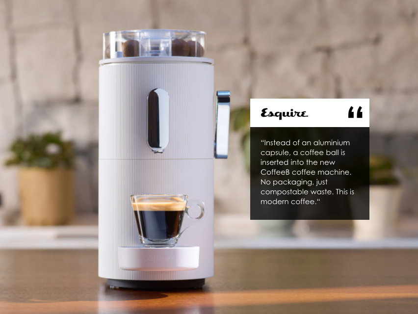Una macchina da caffè bianca con testo di Esquire e una tazza di vetro con caffè.