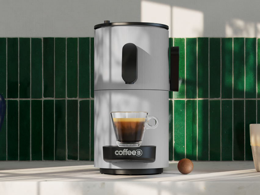Eine silberne Kaffeemaschine mit einer Glastasse unter dem Ausguss. Grüne geflieste Wand im Hintergrund.