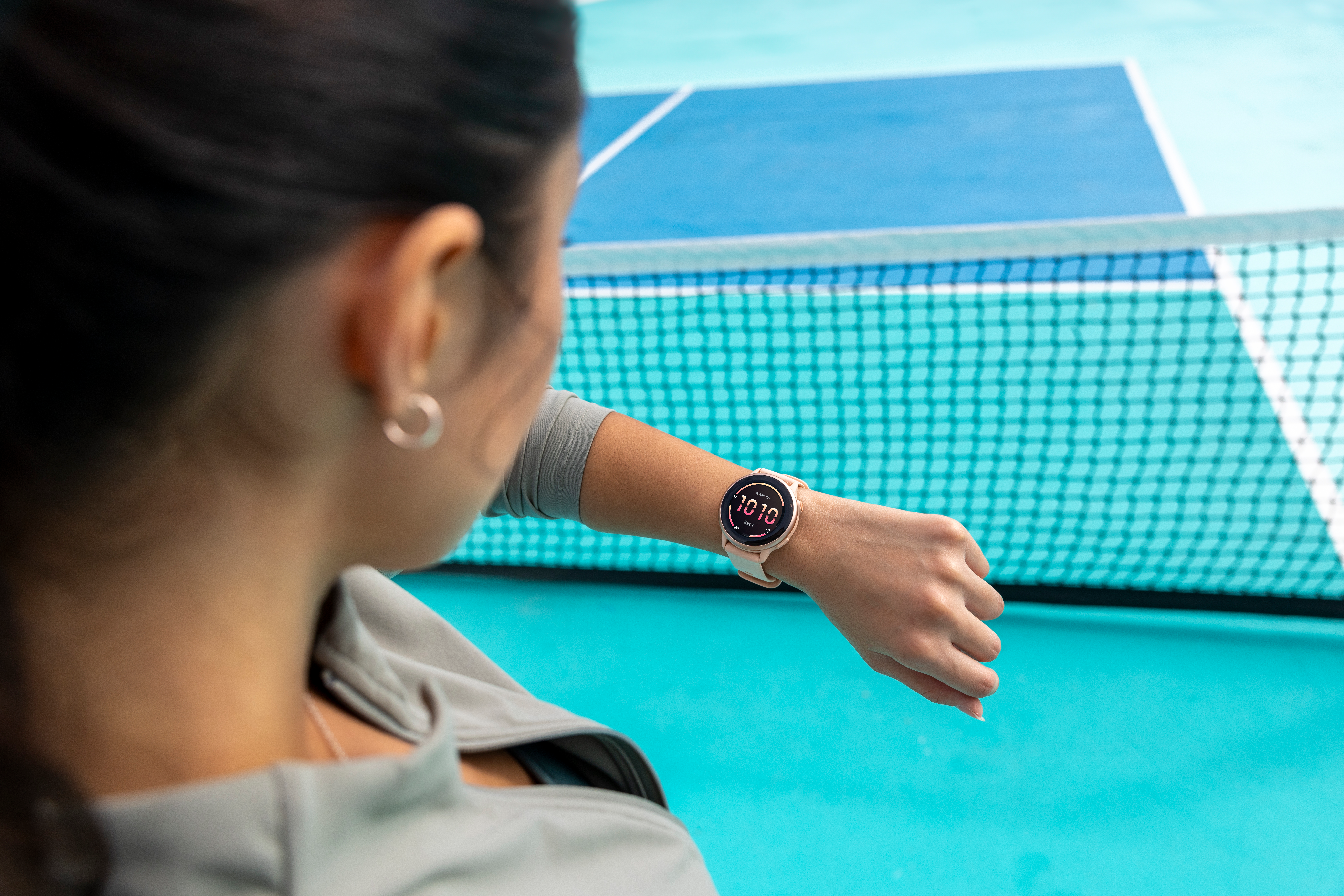Une femme regardant sa montre-bracelet, une smartwatch rose, près d'un filet.