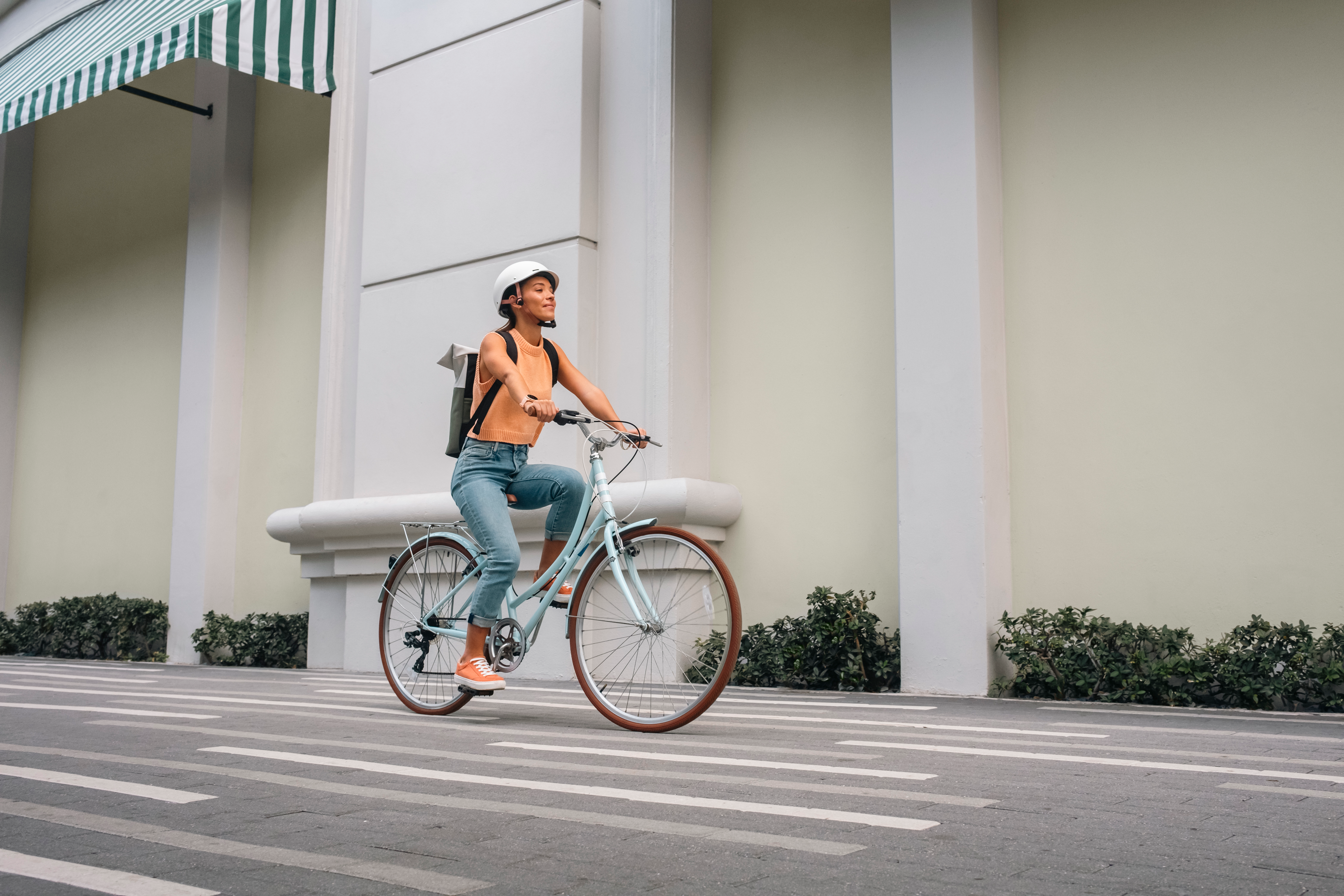 Une femme fait du vélo bleu sur une route, portant un casque. L'arrière-plan montre un bâtiment et de la verdure.