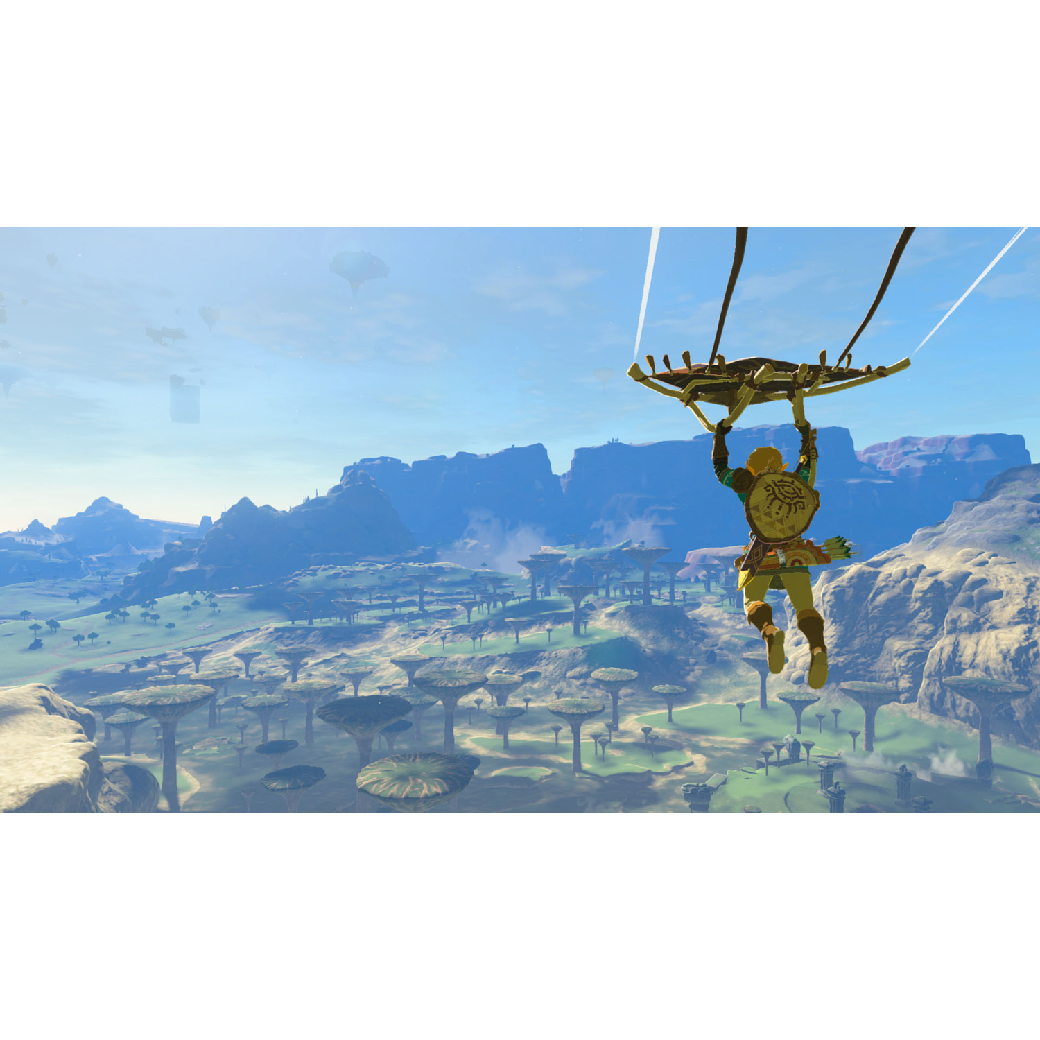 A man is gliding over a green landscape, with a blue sky and mountains.