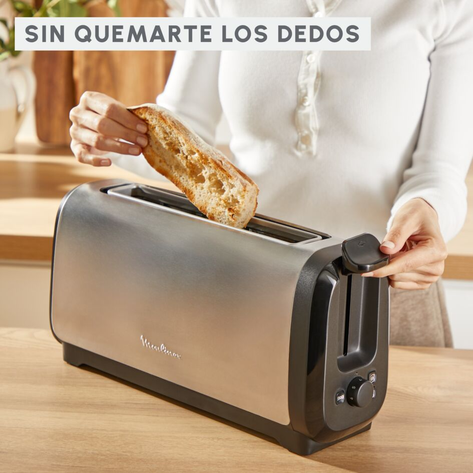Una mujer poniendo pan en una tostadora plateada. La tostadora está sobre una superficie de madera.