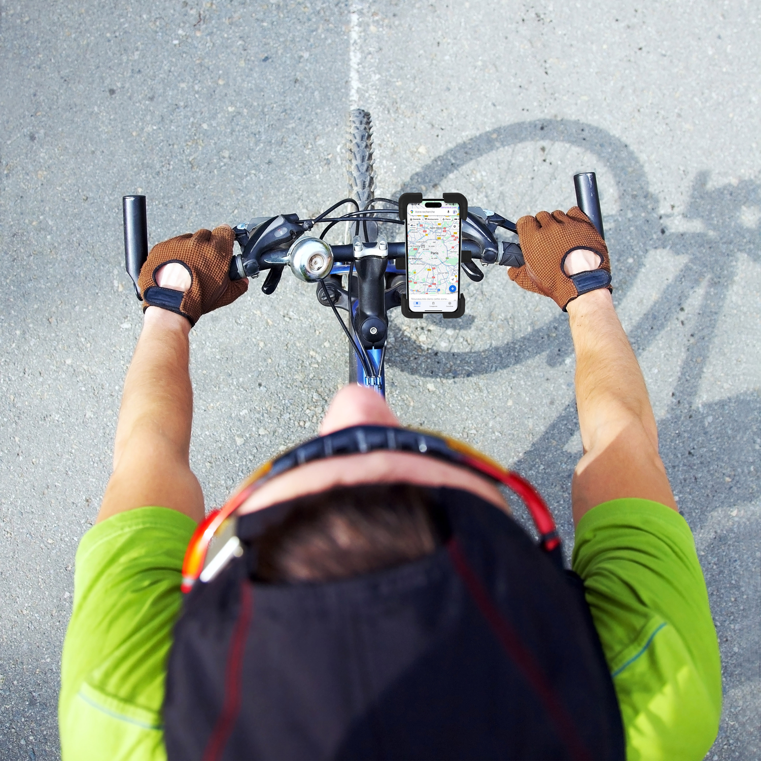 Overhead view of a cyclist with phone on handlebars displaying a map, on gray asphalt.