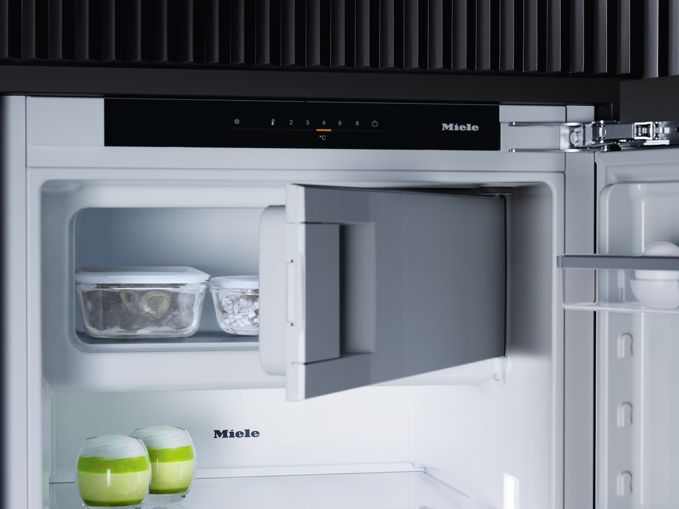 Kühlschrank mit geöffneter Tür, zeigt Lebensmittel und Bedienelemente. Miele-Logo sichtbar.