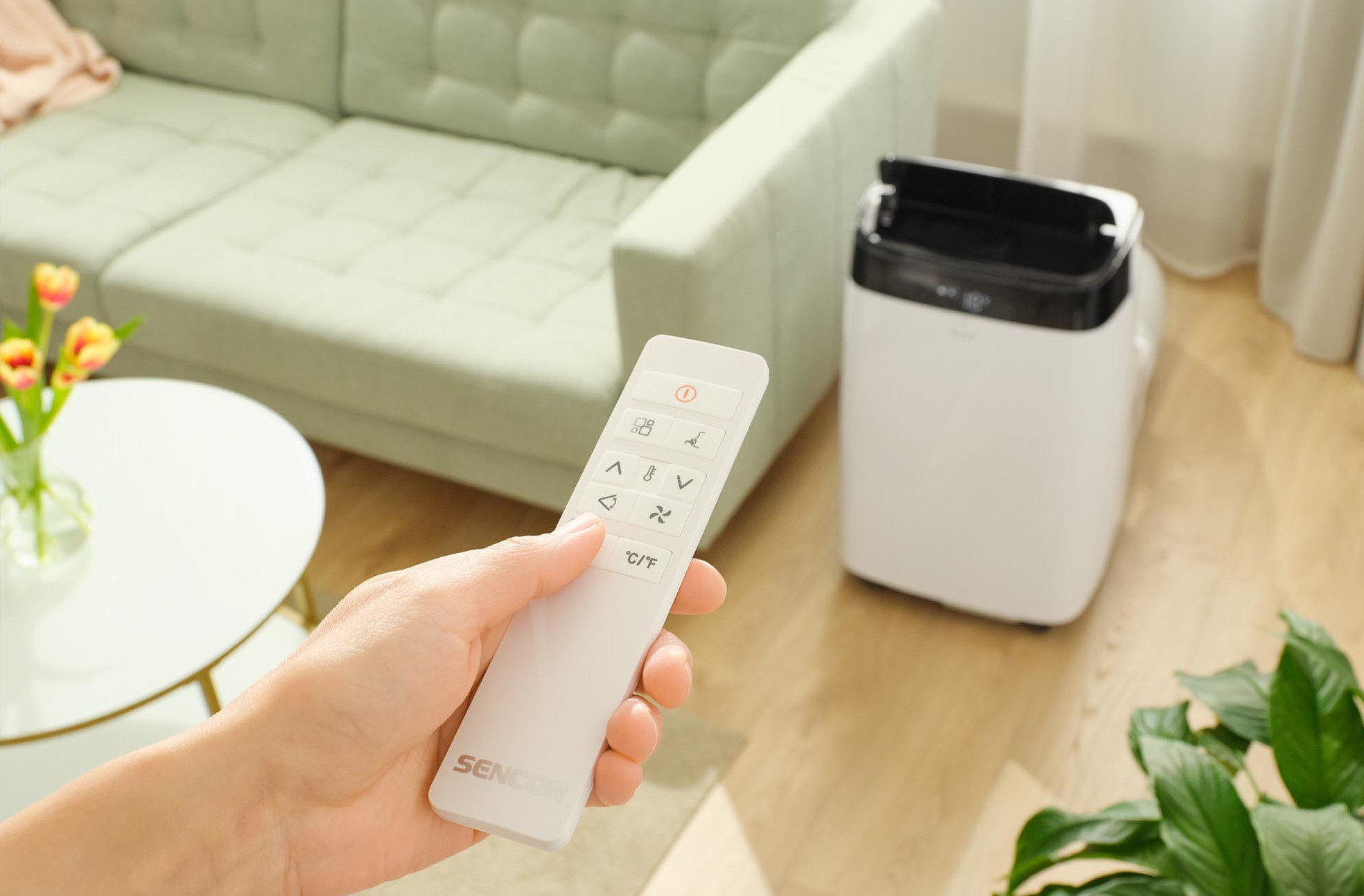 Ręka trzymająca biały pilot w pobliżu klimatyzatora.