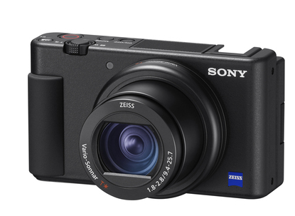 Czarny aparat, widok z góry. Widoczny obiektyw, przyciski i wyświetlacz. Loga SONY i ZEISS.