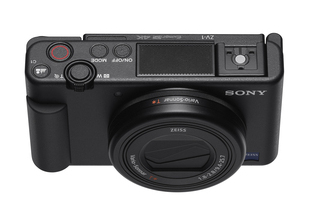 Czarny aparat Sony ZV-1, widok z góry, z przyciskami, obiektywem i widocznym logo Sony, na białym tle.