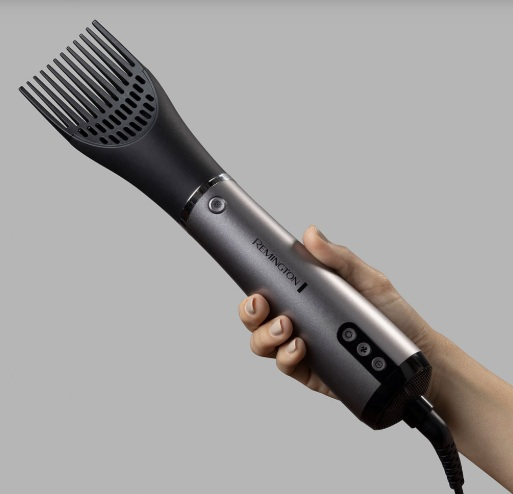 Dłoń trzymająca szarą i czarną suszarkę do włosów Remington z nasadką grzebieniową.