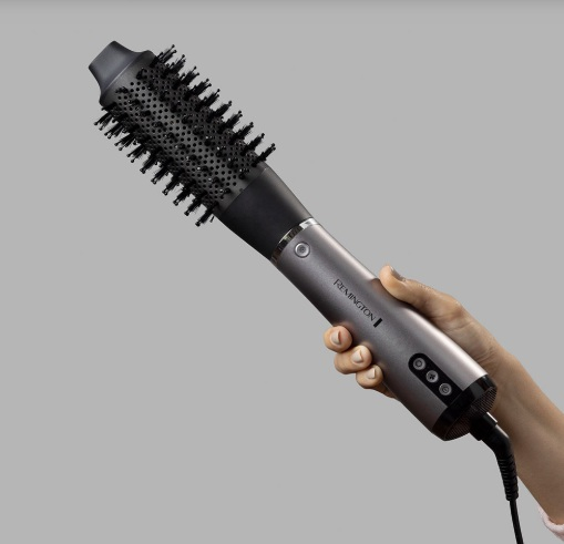 Dłoń osoby trzymającej szczotkę do stylizacji włosów.